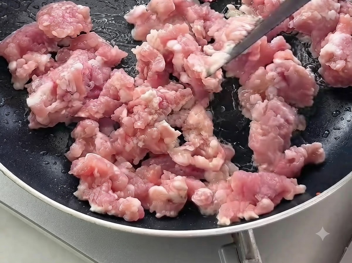 Rohes Schweinehackfleisch wird in einer schwarzen Bratpfanne umgerührt und angebraten.