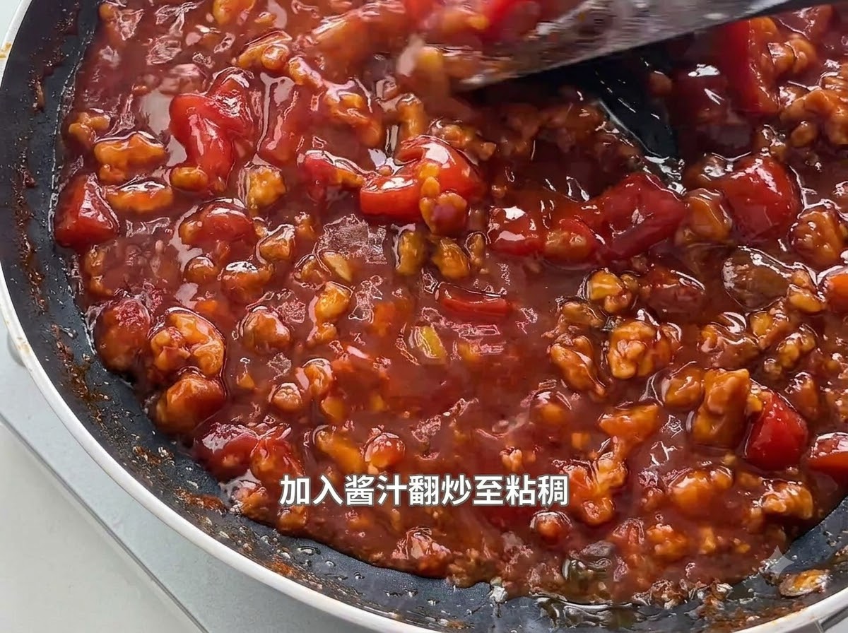 Ein Spatel rührt eine dicke, blubbernde Tomaten-Hackfleisch-Sauce in einer schwarzen Pfanne um.