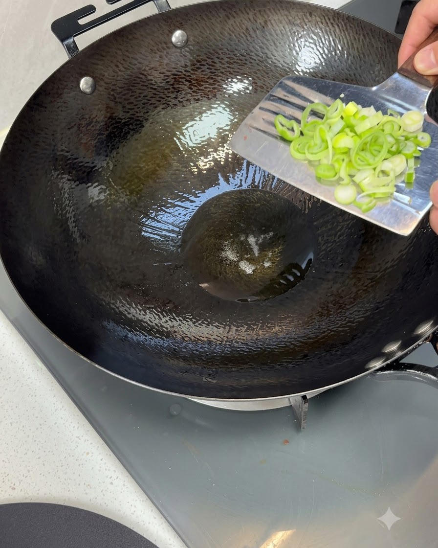 Gehackte Frühlingszwiebeln fallen in einen heißen Wok gefüllt mit schimmerndem Speiseöl.