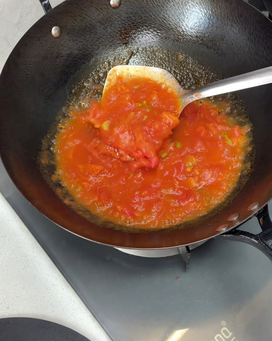 Tomaten werden in einem Wok mit einem Spatel zerdrückt und zu einer reichhaltigen Sauce verrührt.