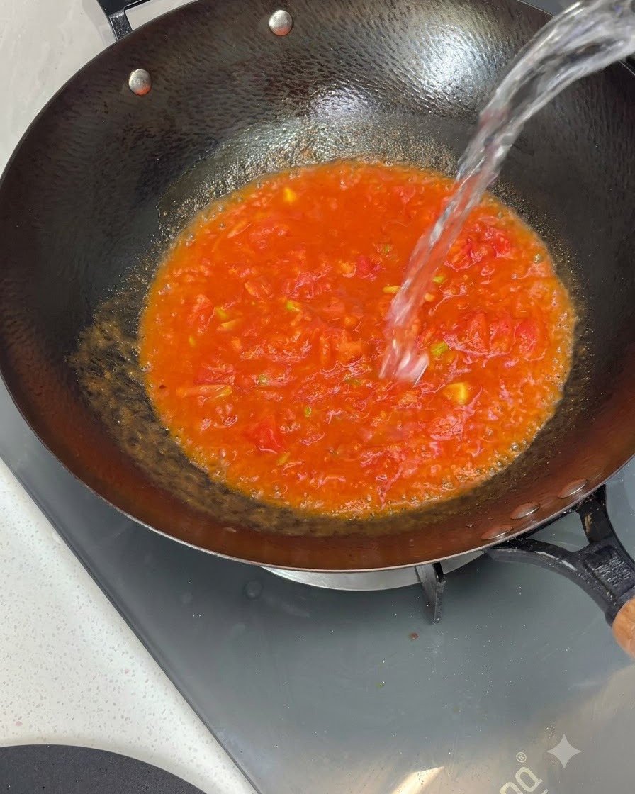 Wasser wird von oben in einen Wok gefüllt, der gekochte Tomatensauce enthält.