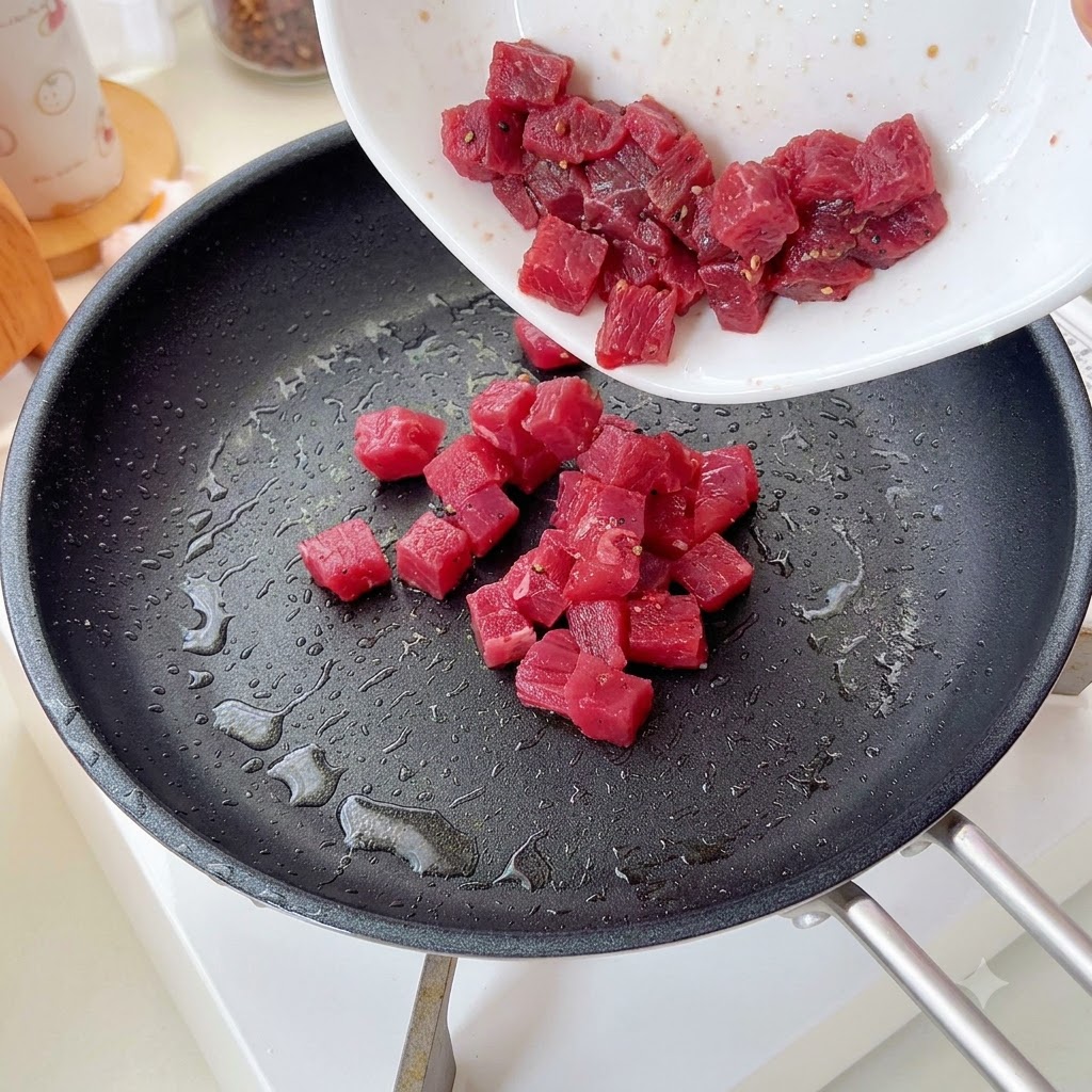 Gewürzte Rindfleischwürfel werden in eine Pfanne gegeben und angebraten.