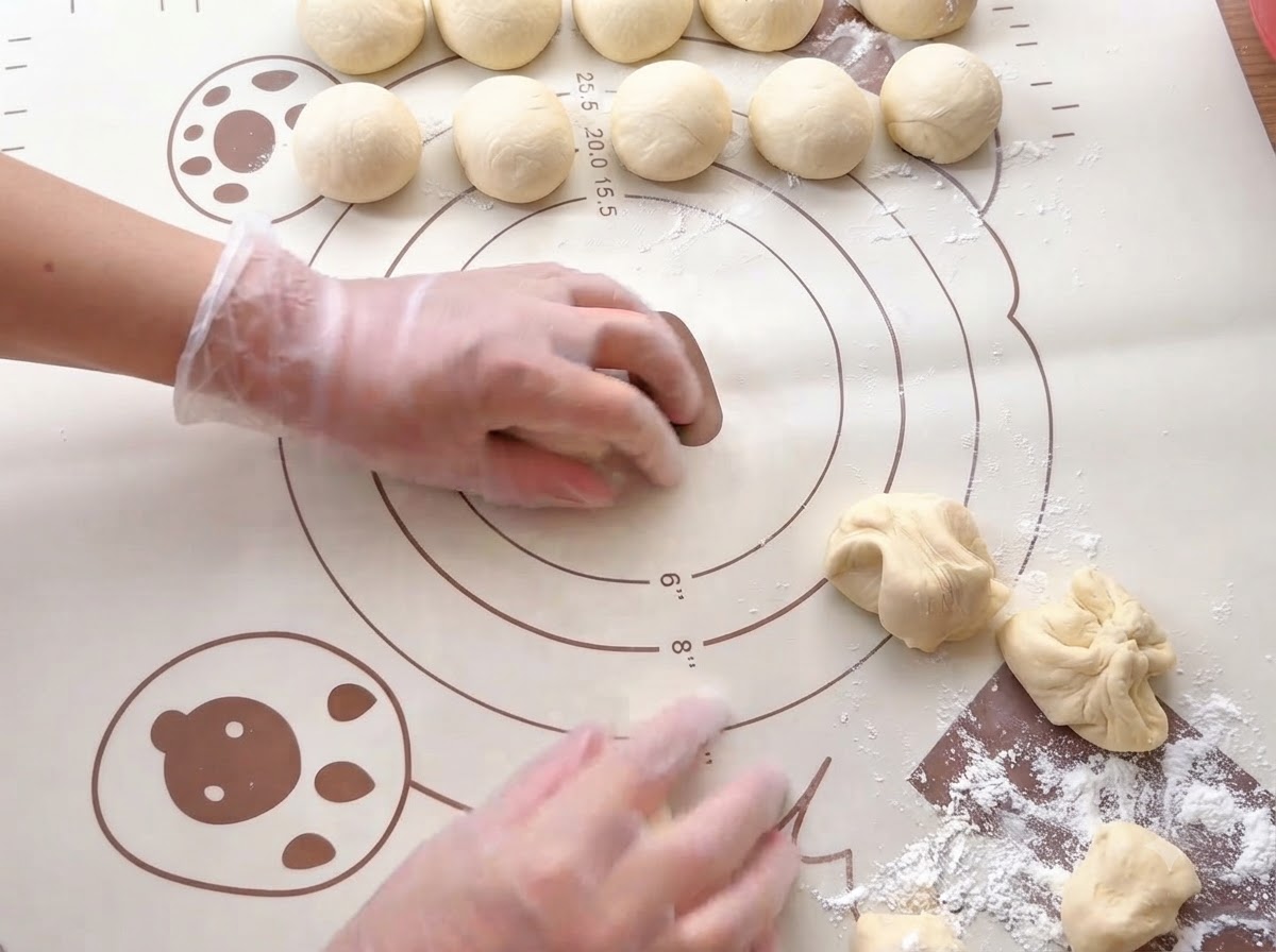 Hände rollen kleine Teigportionen auf einer bedruckten Silikon-Backmatte zu glatten Kugeln.