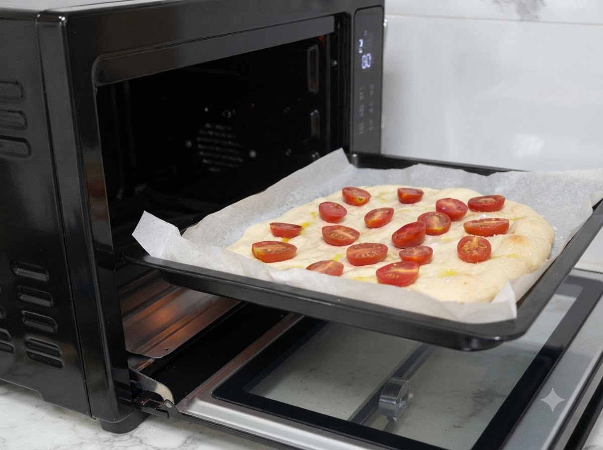 Ein Backblech mit belegtem Pizzateig wird in einen schwarzen Ofen geschoben.
