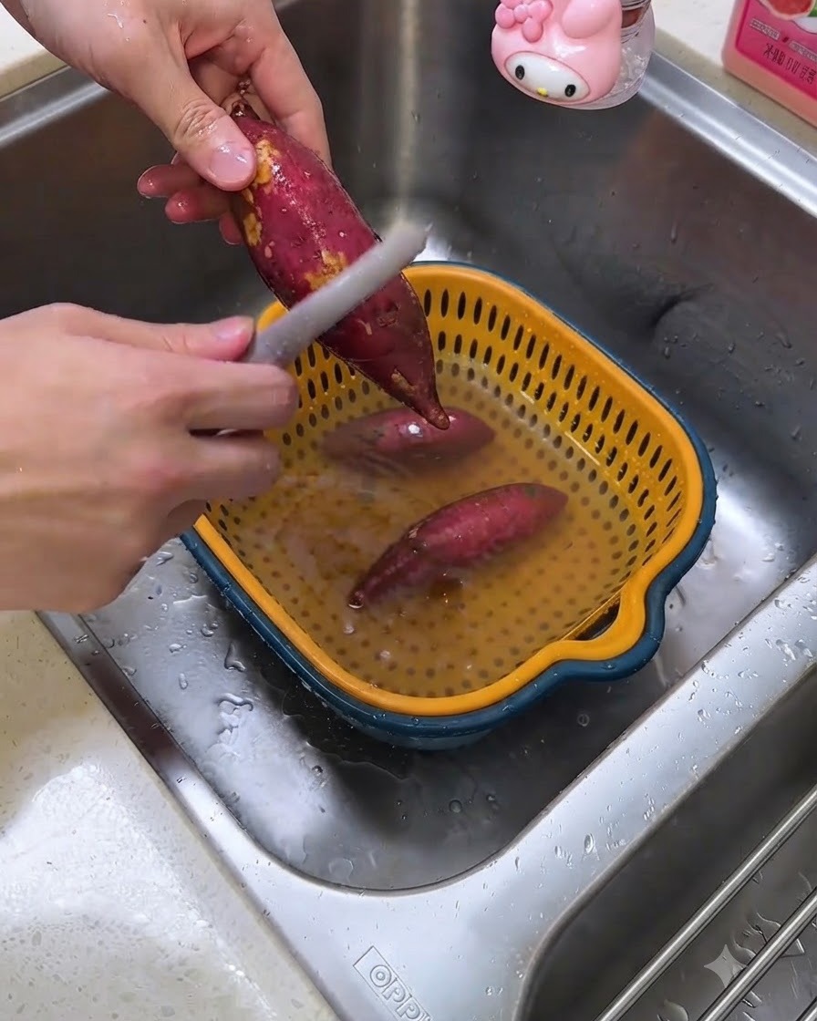 Eine Person schält rohe Süßkartoffeln über einer Spüle mit einem Sparschäler.