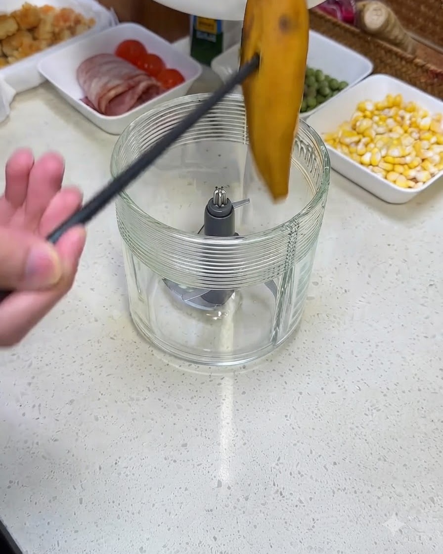 Eine Person legt mit einer schwarzen Zange ein Stück gekochte Süßkartoffel in einen Glasmixerbehälter.