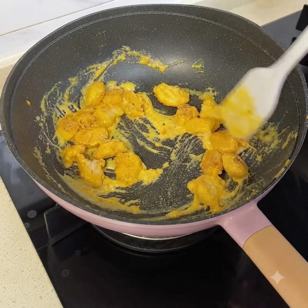 Popcorn-Hähnchenstücke werden mit einem Silikonspatel in einer Pfanne mit gelber Eigelbsauce verrührt und umhüllt.