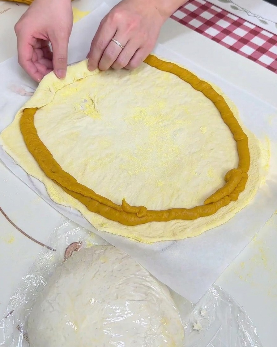 Hände falten den Teigrand über den aufgespritzten Süßkartoffelpüree-Ring auf Backpapier.