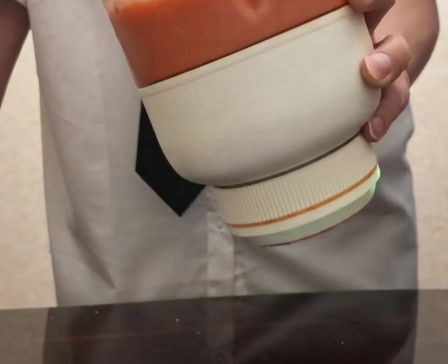 Eine Person hält einen tragbaren elektrischen Blender, gefüllt mit glattem, hellrotem Tomatenpüree.