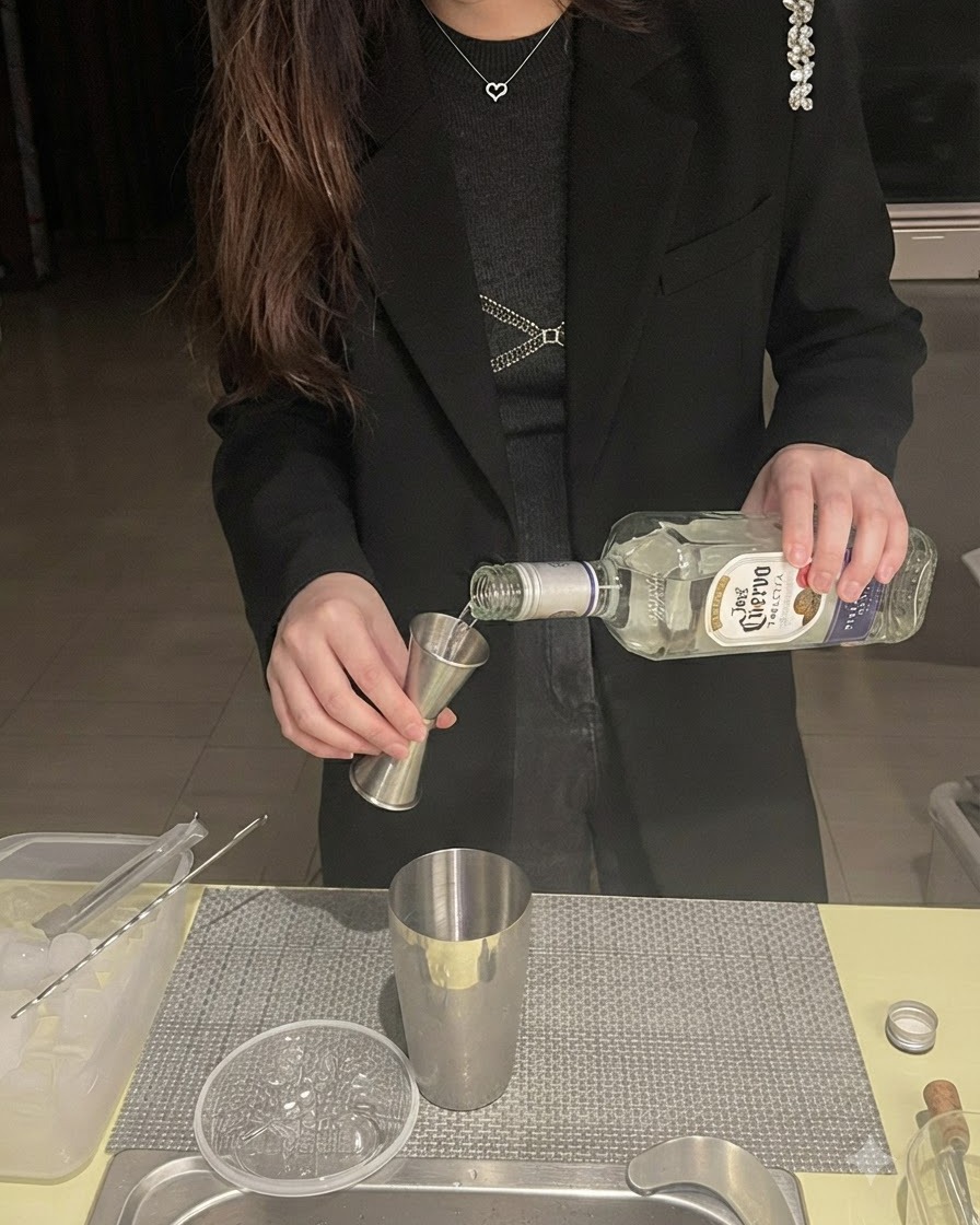 Tequila, der aus einer Flasche in einen Jigger über einem metallenen Shaker gegossen wird.