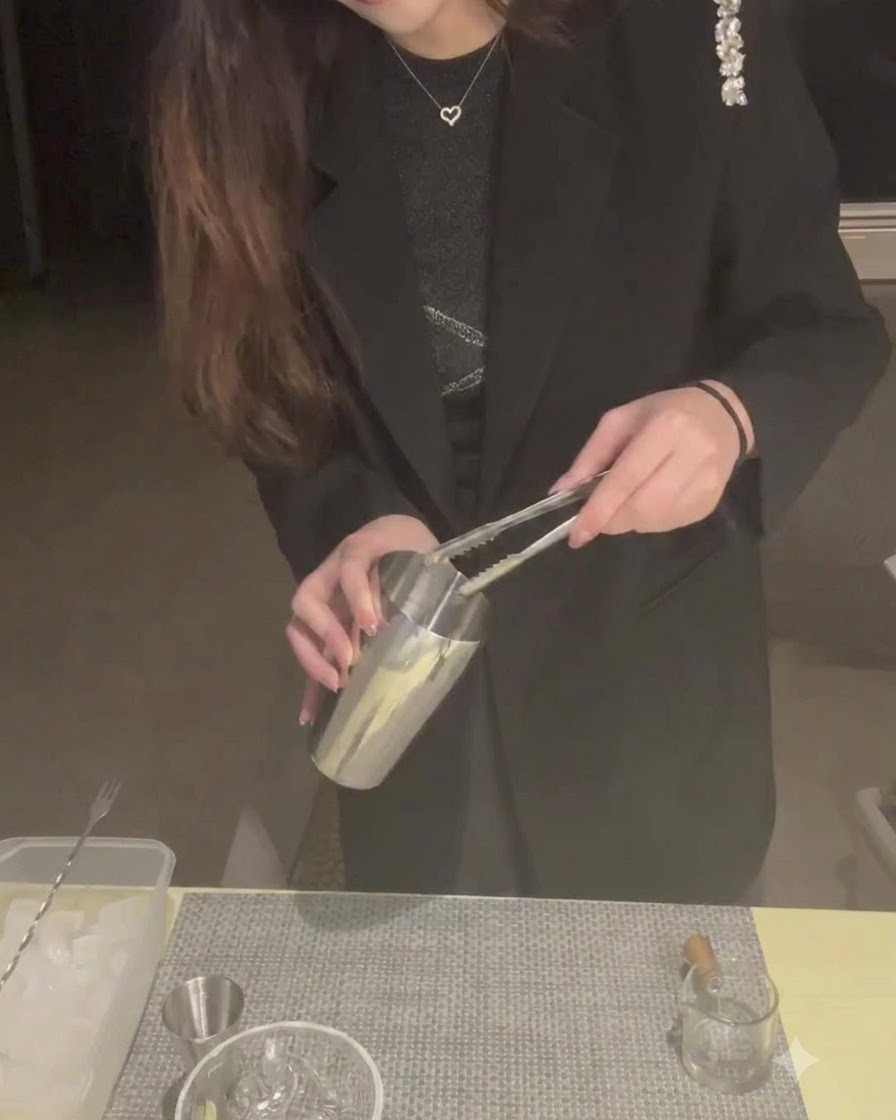 Eine Person verwendet eine Zange, um Eiswürfel in einen Cocktailshaker aus Metall zu geben.