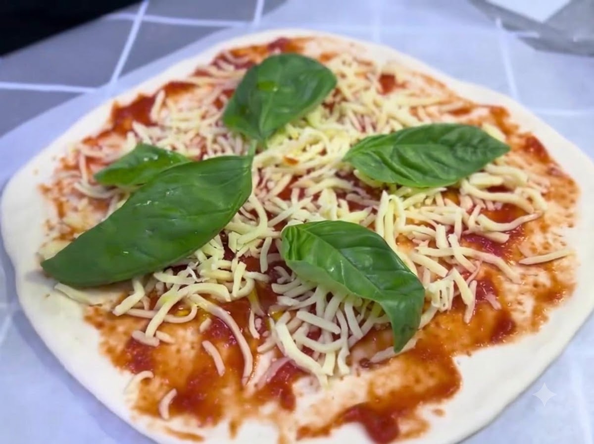Eine belegte Pizza mit Käse und Basilikumblättern erhält einen leichten Spritzer Olivenöl.