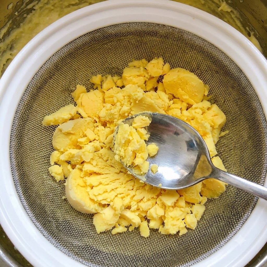 Gekochte Eigelbe werden mit einem Löffel durch ein Drahtsieb gedrückt.