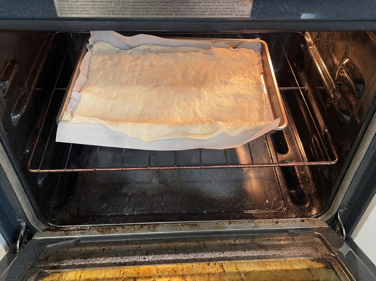 Ein Backblech mit rohem Pizzateig auf Backpapier im vorgeheizten Ofen auf dem Rost.