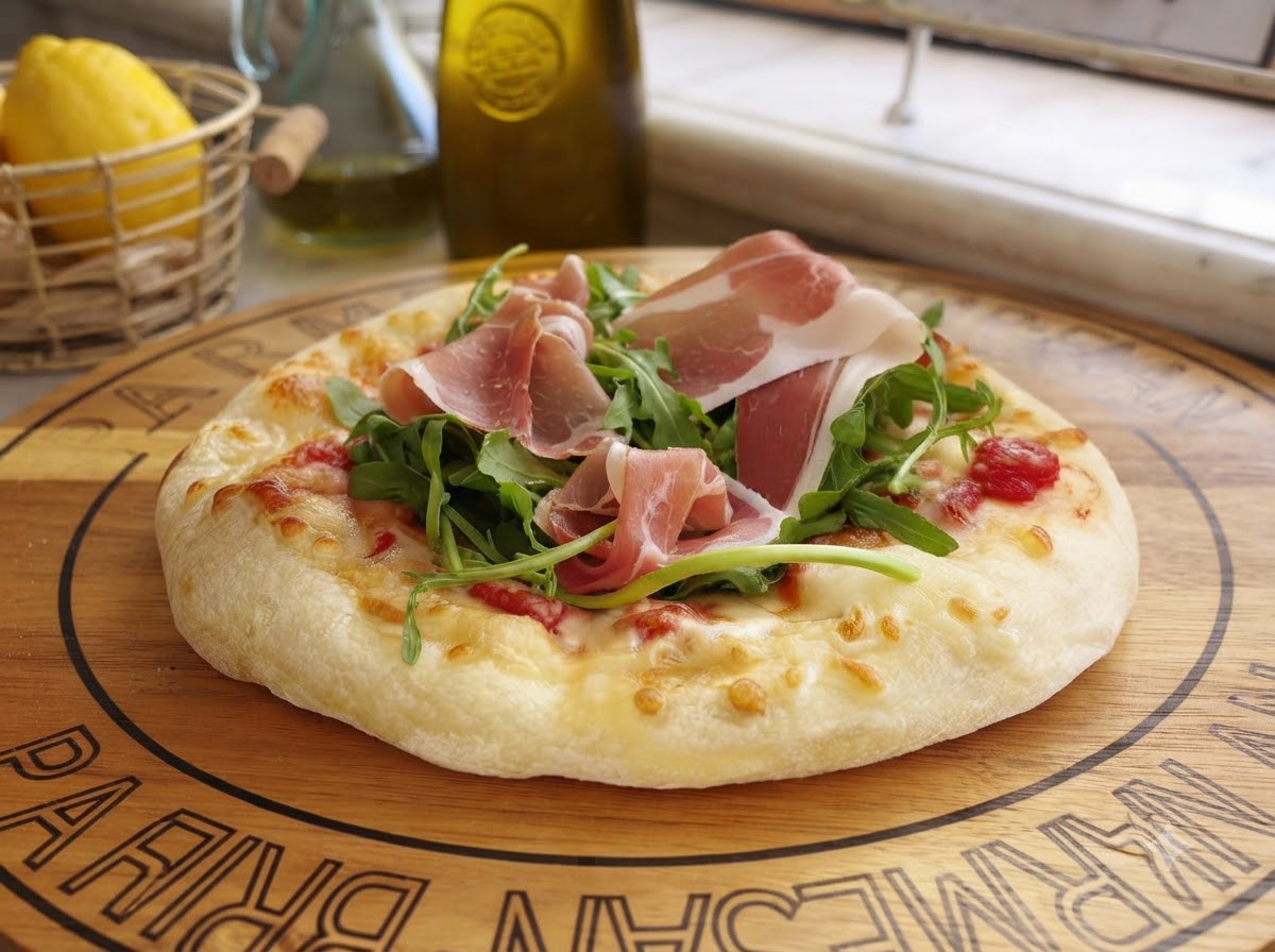 Frisch gehobelter Parmesankäse fällt auf eine fertige Pizza, die mit Grünzeug und Wurstwaren belegt ist.