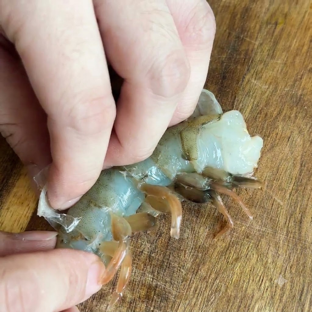 Finger ziehen die durchsichtige Schale von einer rohen Garnele auf einer Holzoberfläche ab.