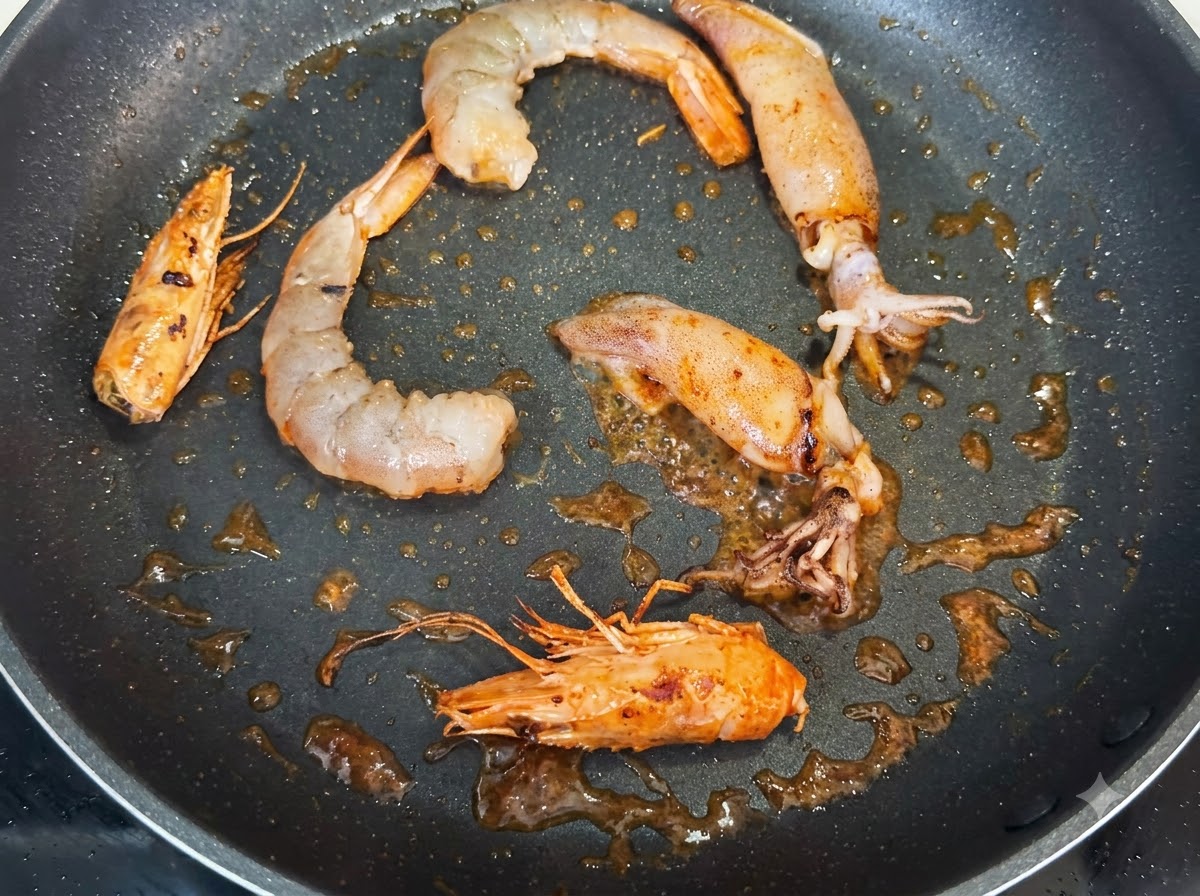 Garnelen, ganze Garnelenköpfe und Tintenfischstücke braten in einer Pfanne, gewürzt mit dunklen Punkten schwarzem Pfeffers.