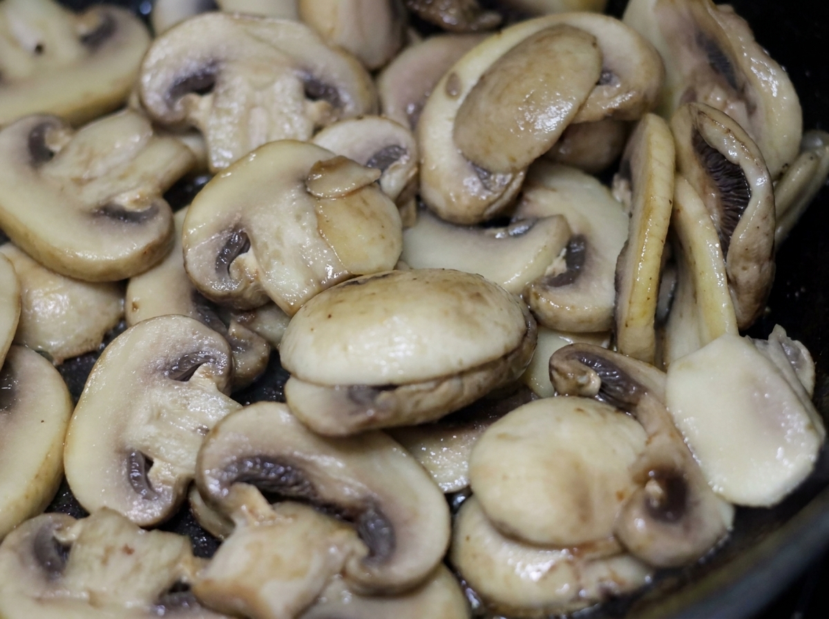 In Scheiben geschnittene weiße Champignons brutzeln mit leichter Sahne in einer Pfanne.