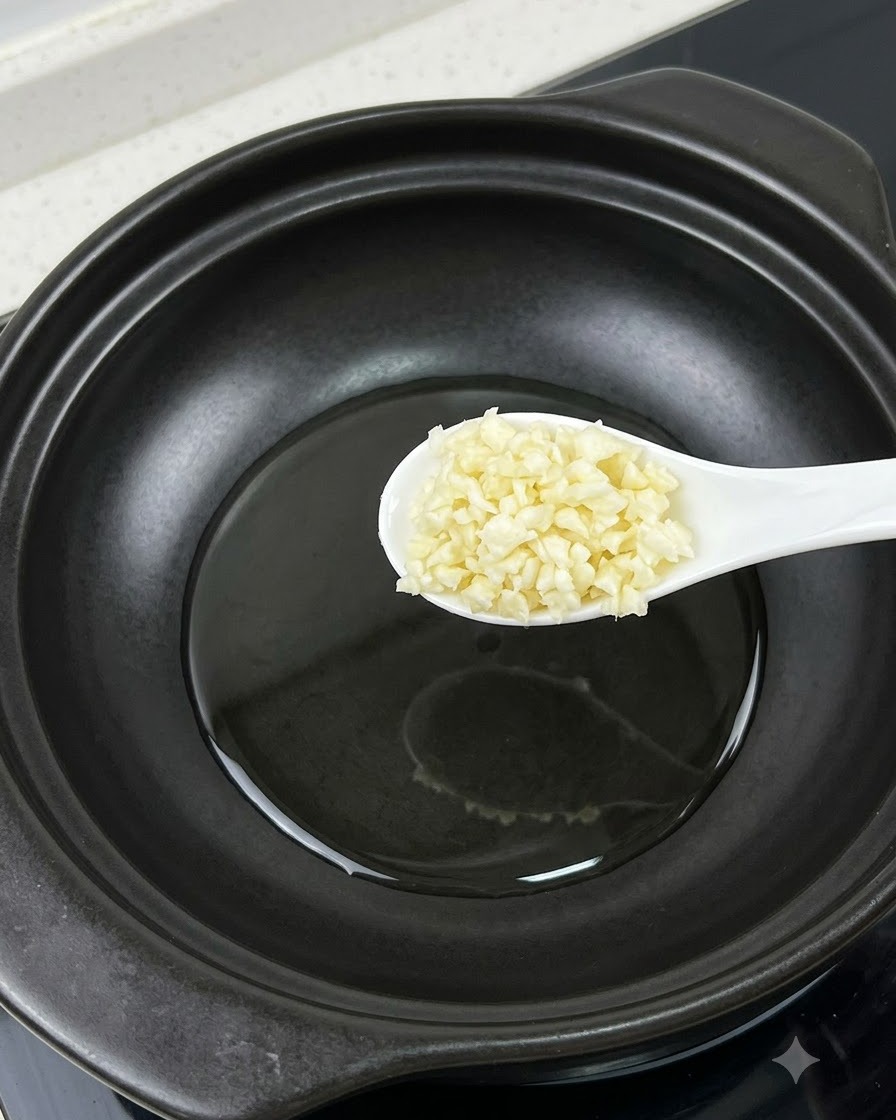 Ein Löffel gehackter Knoblauch wird über einen Topf neben einem getrennten Eigelb gehalten.