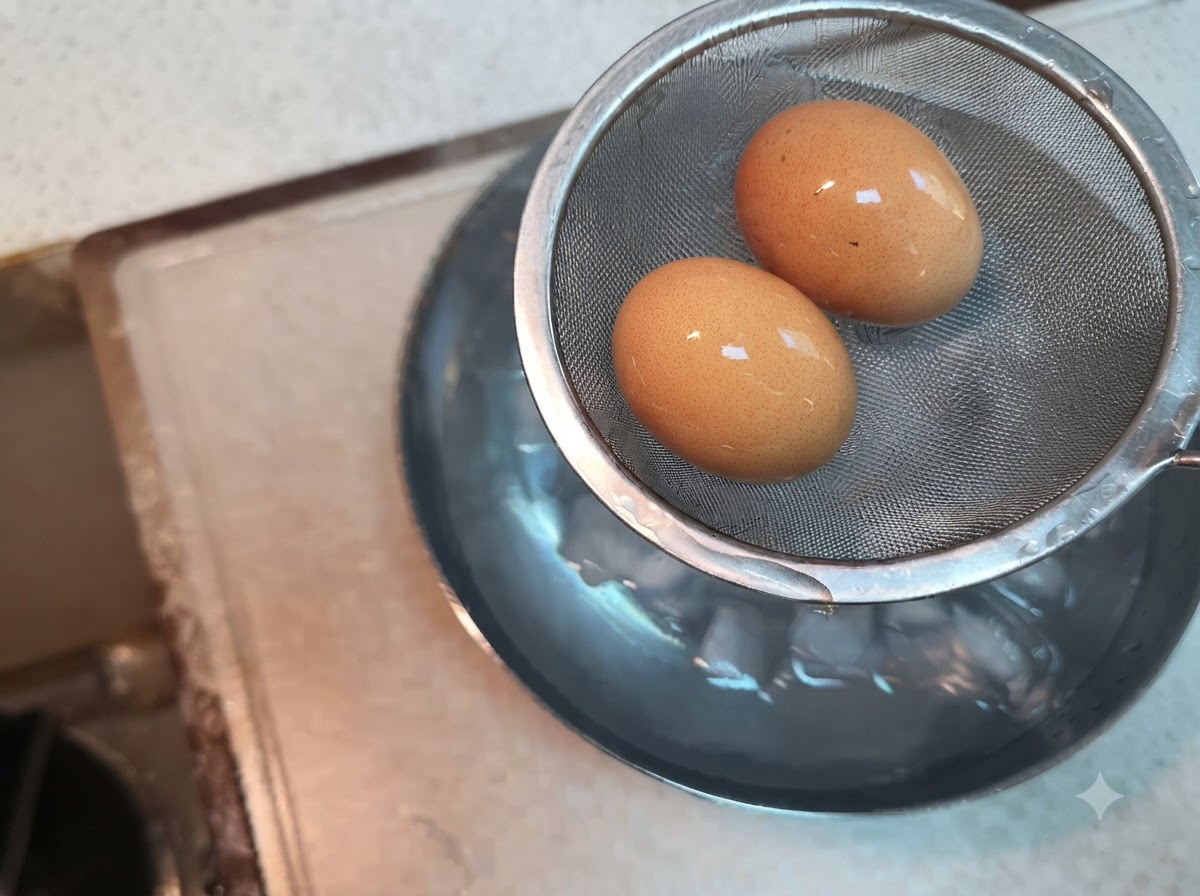 Zwei gekochte Eier liegen in einem Drahtsieb, das über eine Schüssel mit Eiswasser gehalten wird.