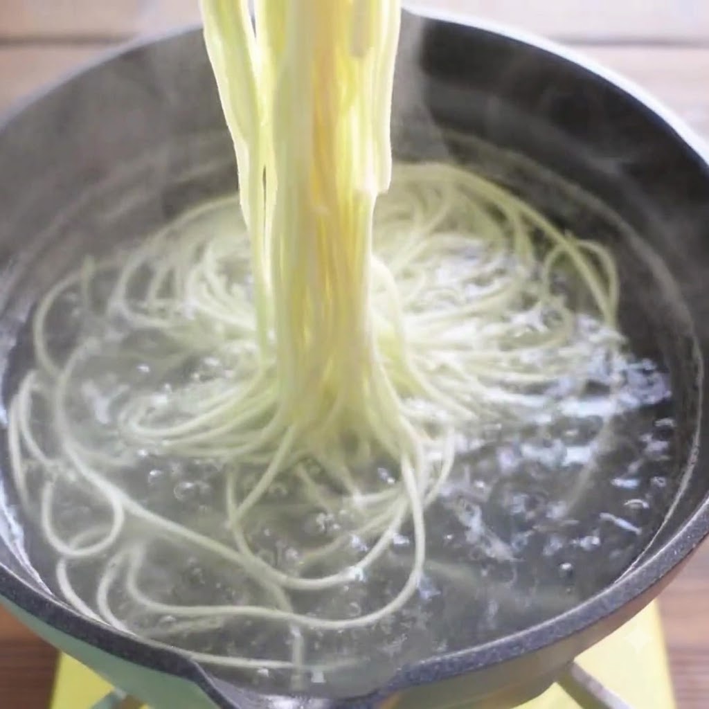 Essstaebchen heben gekochte Ramen-Nudeln aus dem kochenden Wasser.
