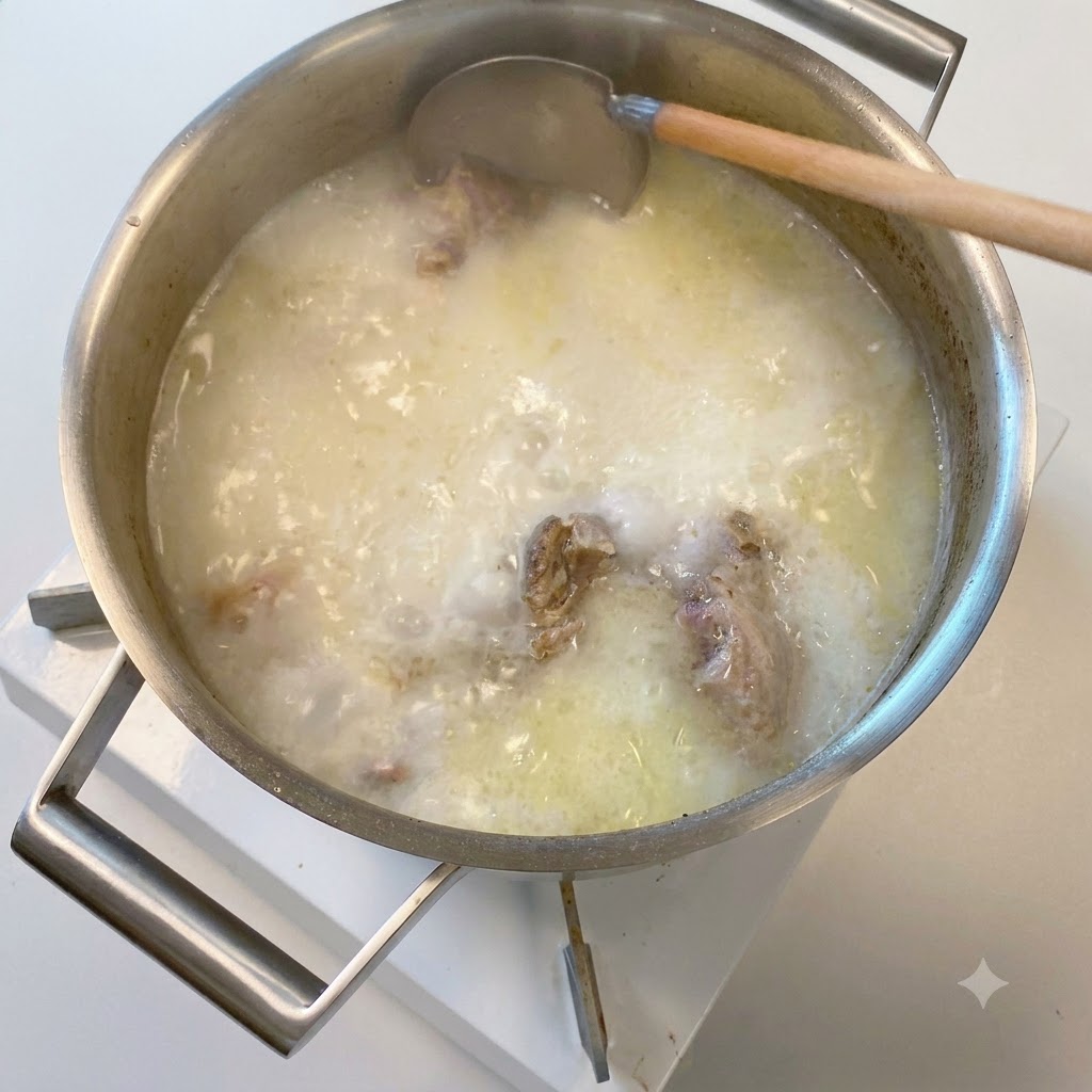 Eine Holzkelle taucht in einen Topf mit undurchsichtiger, milchig weißer, köchelnder Schweineknochenbrühe.