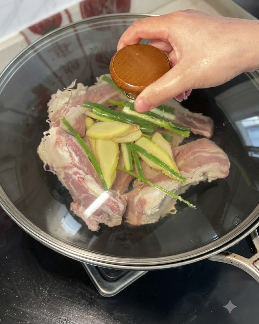 Eine Hand gießt Gelbwein über Rinderrippchen, Ingwer und Frühlingszwiebeln in einem Wok.