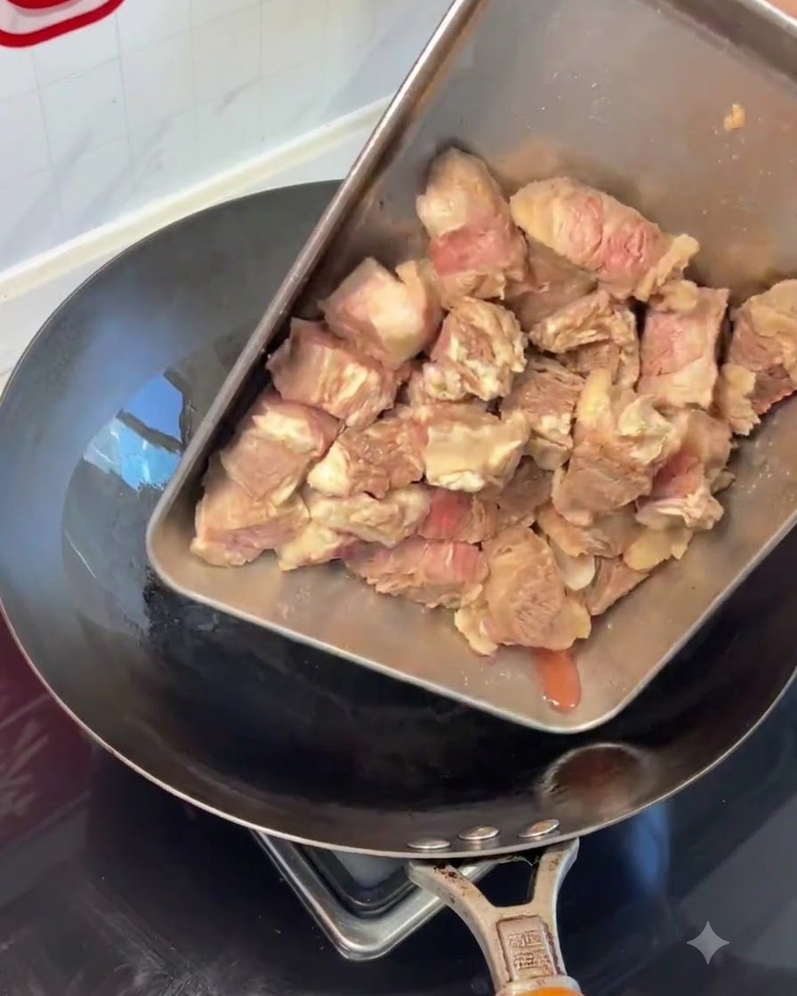 Blanchierte Rinderrippchenstücke werden von einem Tablett in einen heißen Wok gegeben.