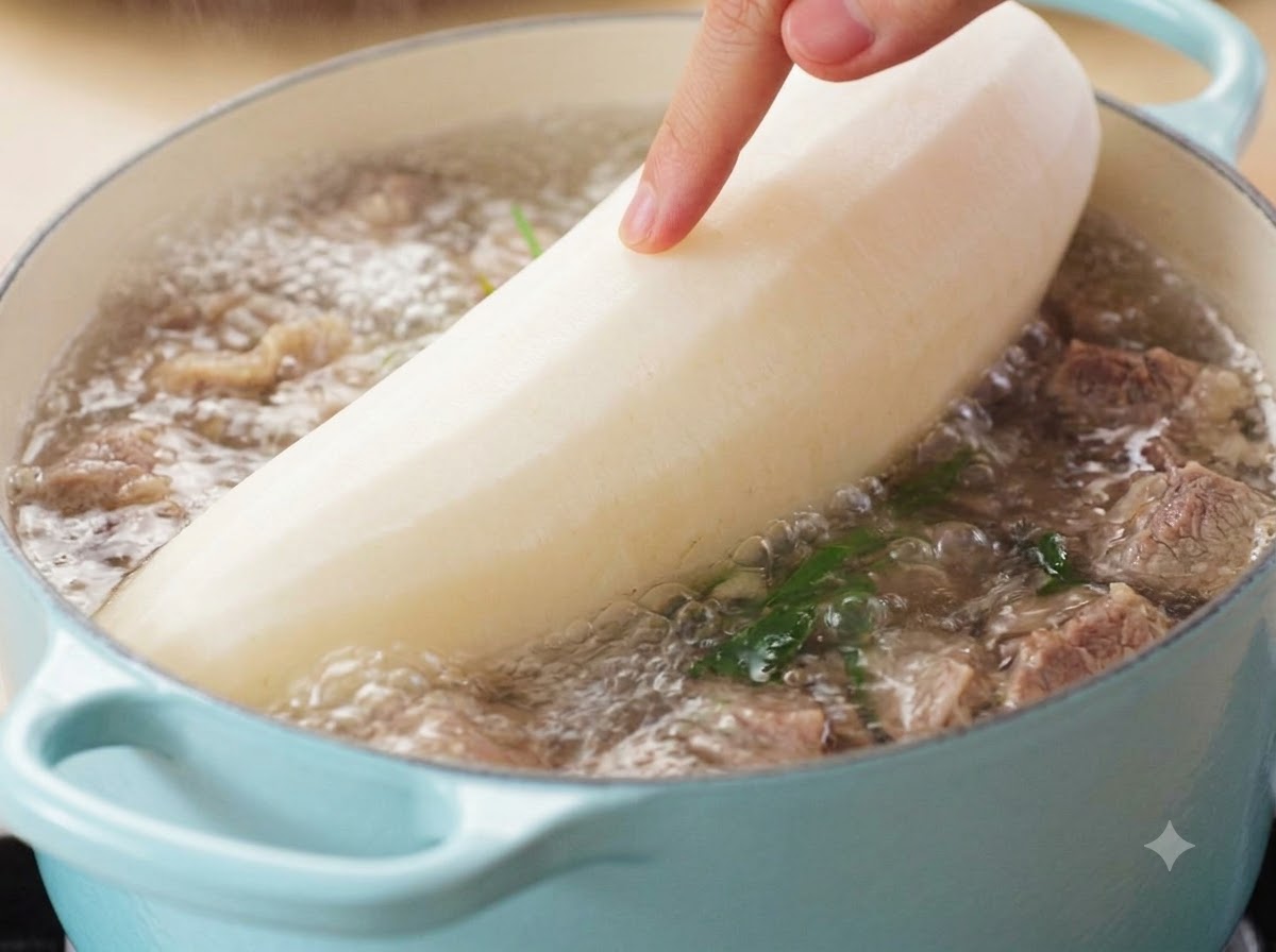 Eine Hand führt einen großen, geschälten weißen Rettich in einen blubbernden Topf mit Rindersuppe.