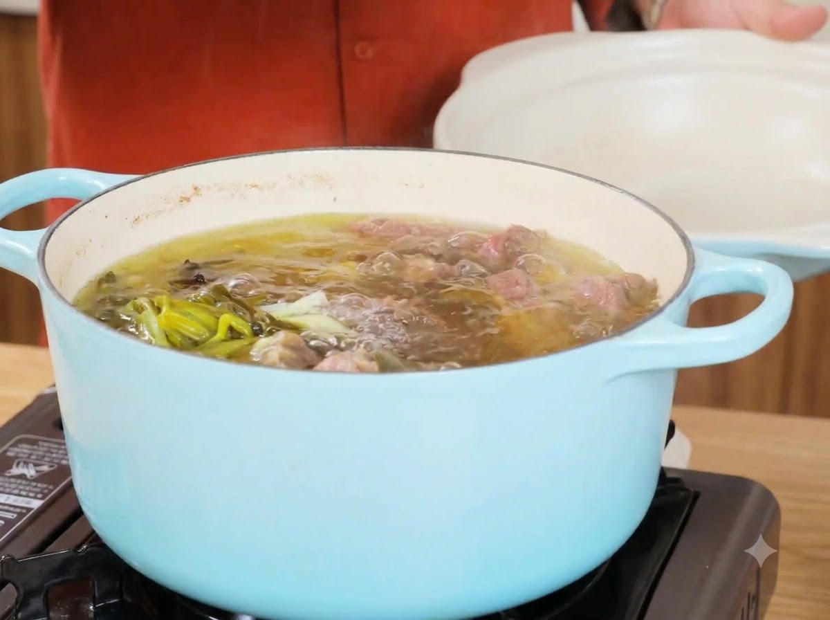 Ein Topf mit simmering Rinderbrühe nach dem Entfernen der Hauptzutaten, mit klarer Flüssigkeit und Frühlingszwiebeln.