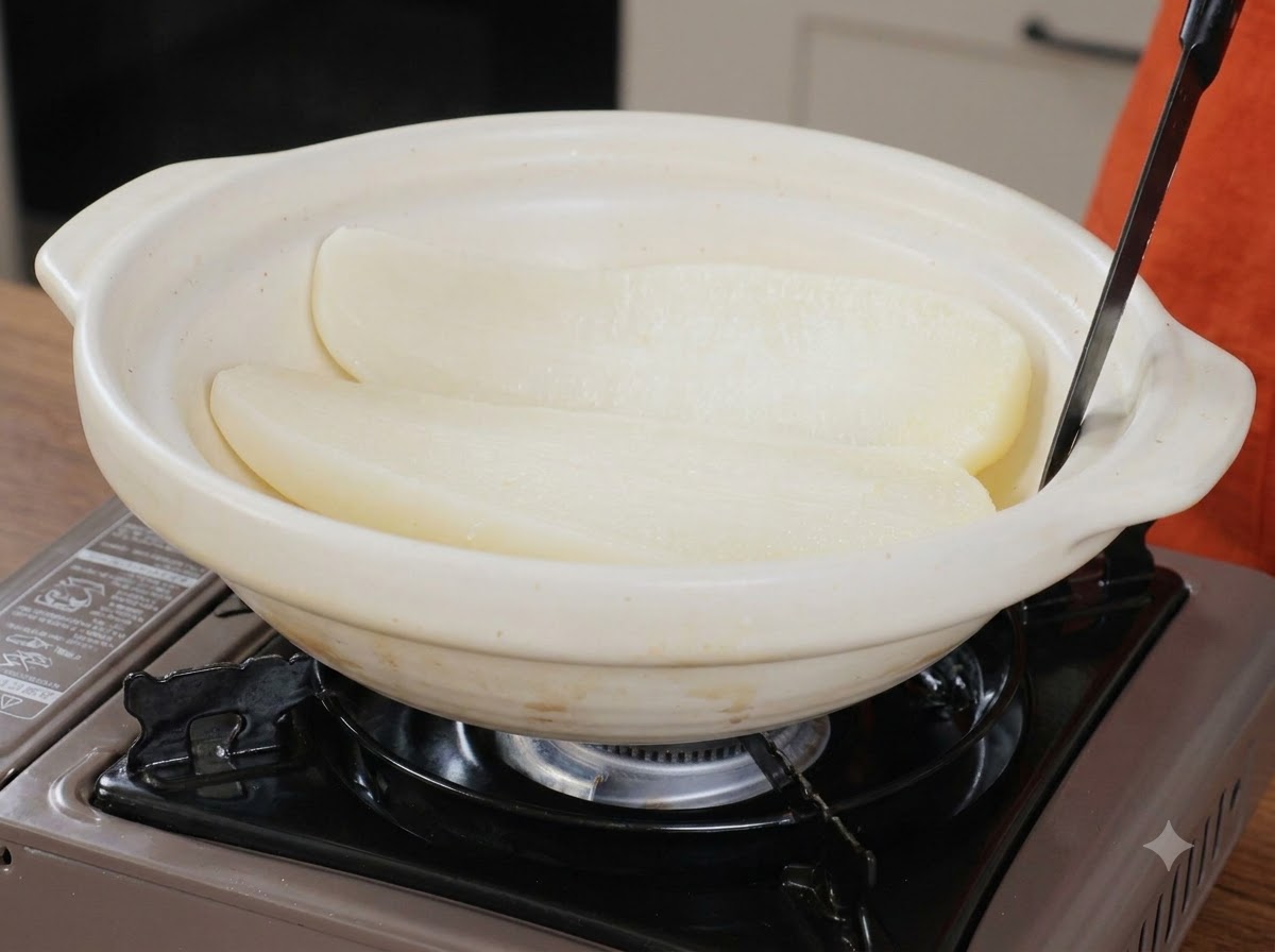 Zwei Hälften gekochten weißen Rettichs liegen in einem breiten weißen Keramik-Serviertopf mit einem Utensil.