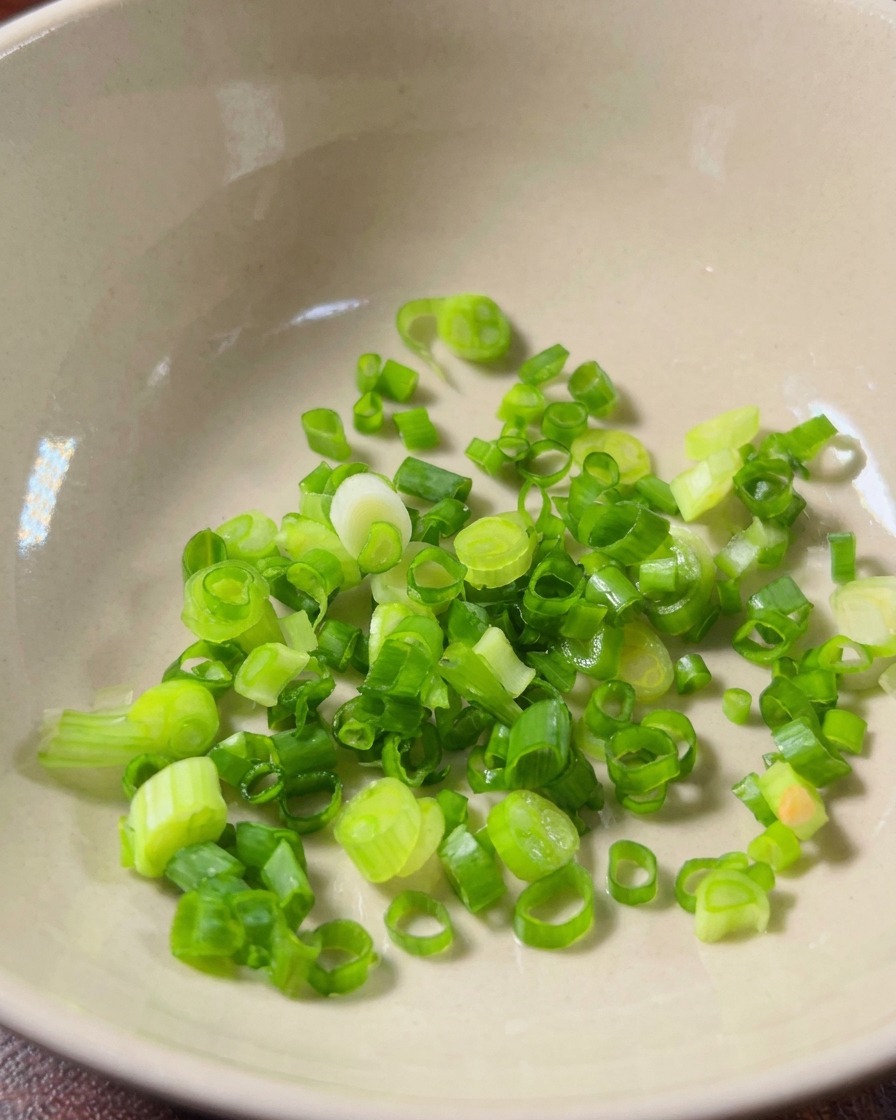 Fein gehackter Knoblauch und frische rote Hirse-Chilischeiben in einer sauberen Keramikschüssel.