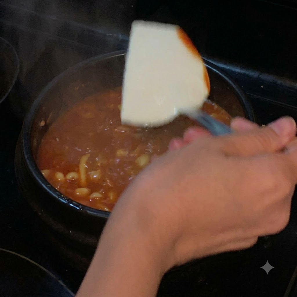 Ein Stück weicher Tofu wird mit einem Spatel in die kochende rote Suppe gesenkt.