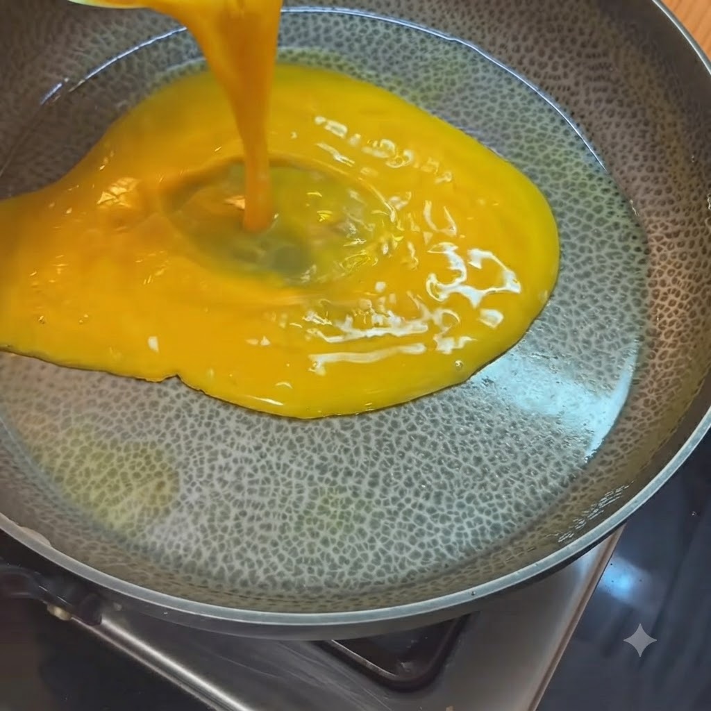 Hellgelbe verquirlte Eier werden aus einem Messbecher in eine heiße, geölte Pfanne gegossen.