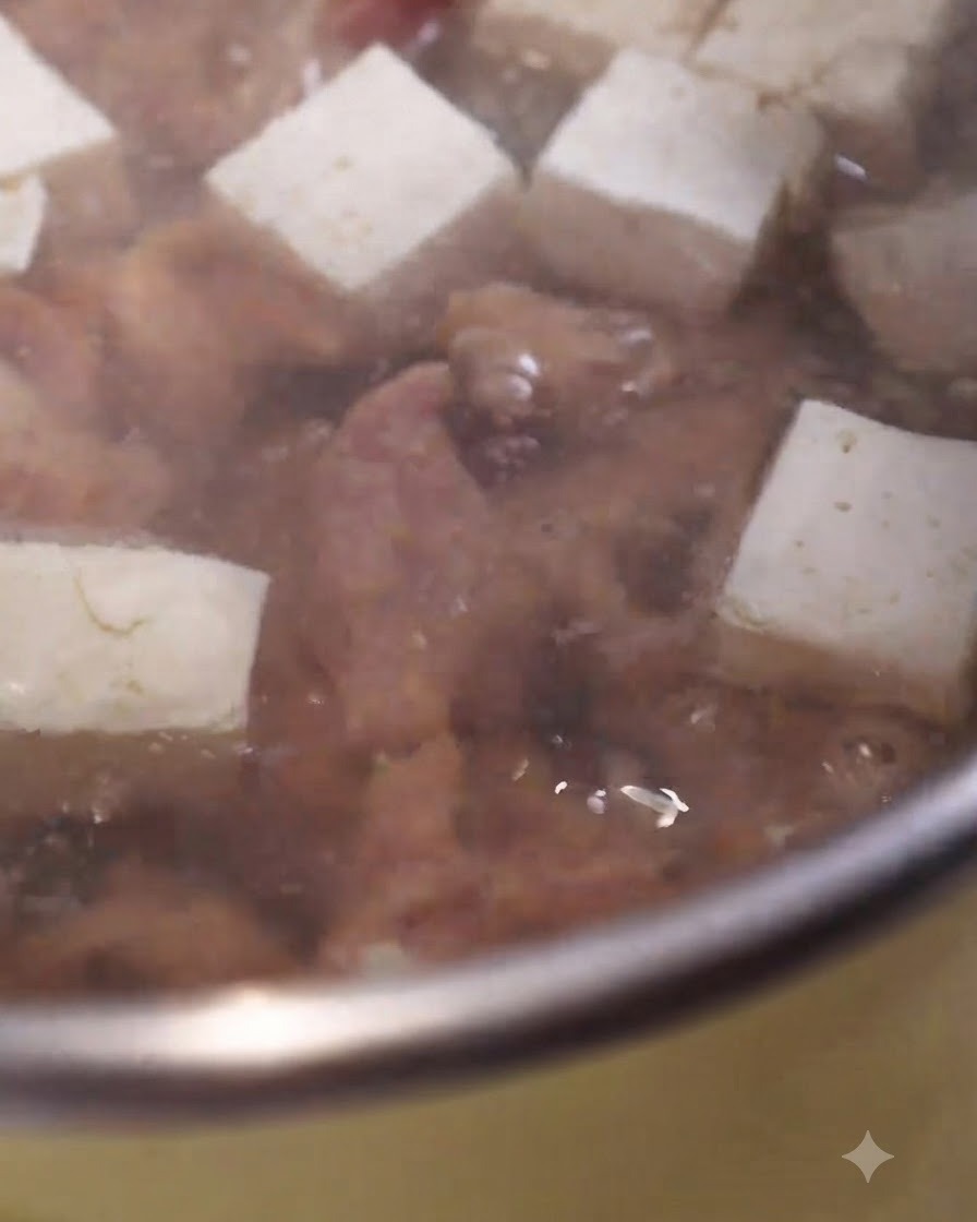 Marinierte Schweinefleischscheiben kochen in einem blubbernden Suppentopf neben weißen Tofuwürfeln.