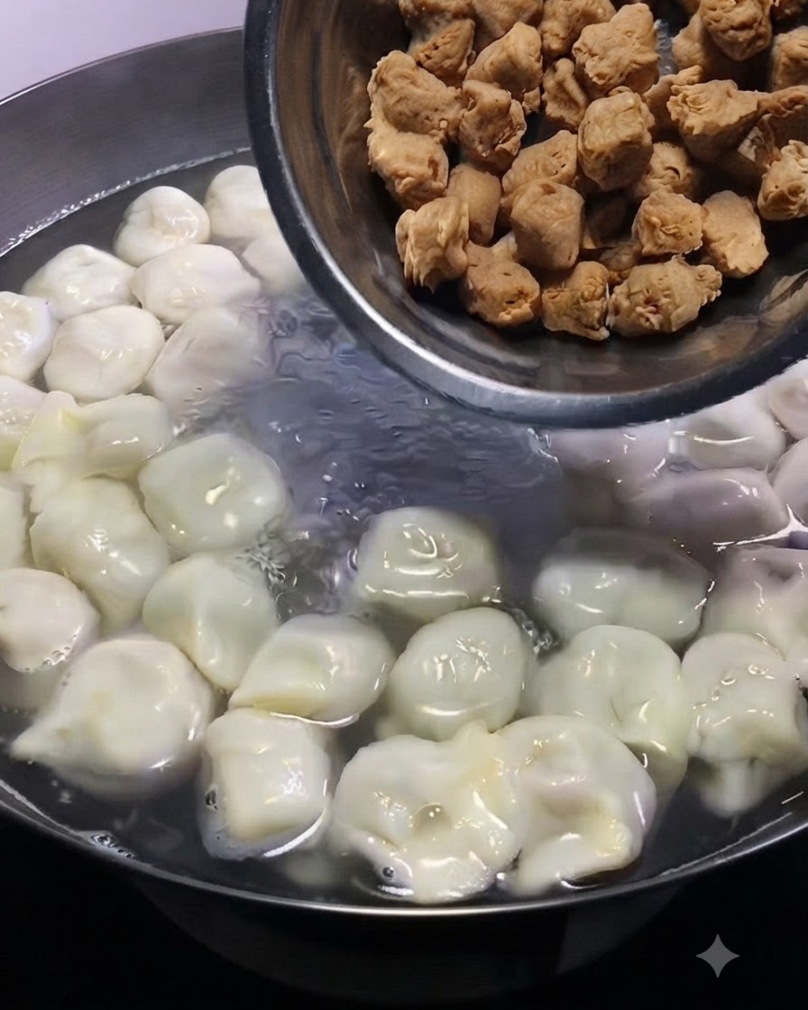 Kleine braune Fleischbällchen werden aus einer Metallschüssel in einen simmernden Topf mit Teigtaschen geschüttet.