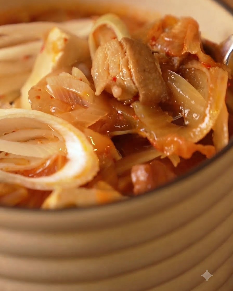 Nahaufnahme einer heißen Kimchisuppe mit Zwiebeln, Tofu und Schweinefleisch in einer Servierschüssel.
