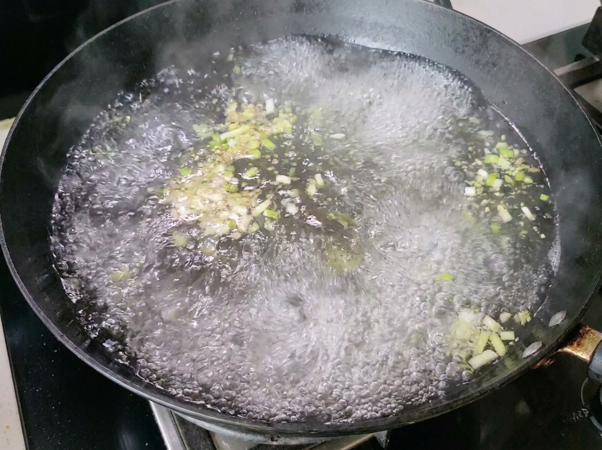 Kochendes Wasser mit Frühlingszwiebeln und Ingwer erzeugt Dampf im Wok.