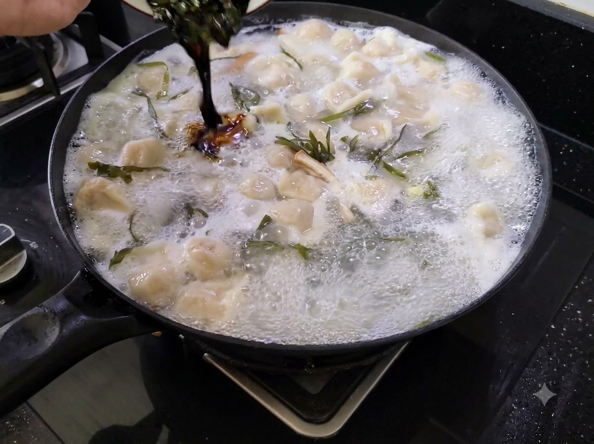 Dunkle Würzsauce wird aus einer kleinen Schüssel in einen großen Topf mit kochender Teigtaschensuppe gegossen.