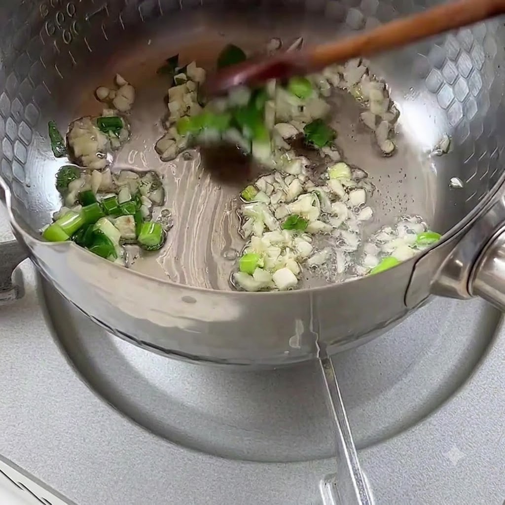 Gehackte Frühlingszwiebeln und Knoblauch brutzeln in Speiseöl in einem Metalltopf.