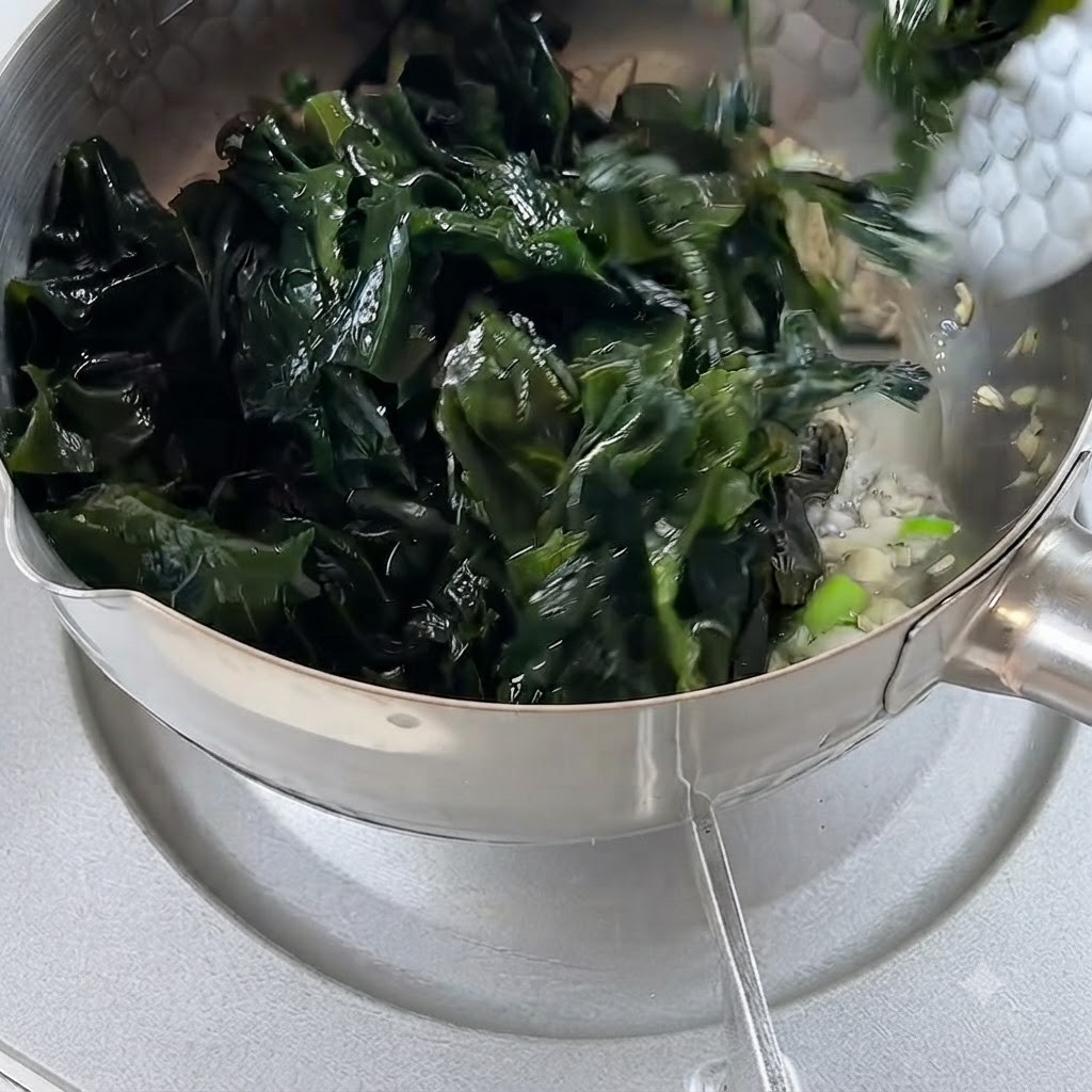 Eingeweichte Algen werden in den Topf mit gebratenem Knoblauch und Zwiebeln gegeben.