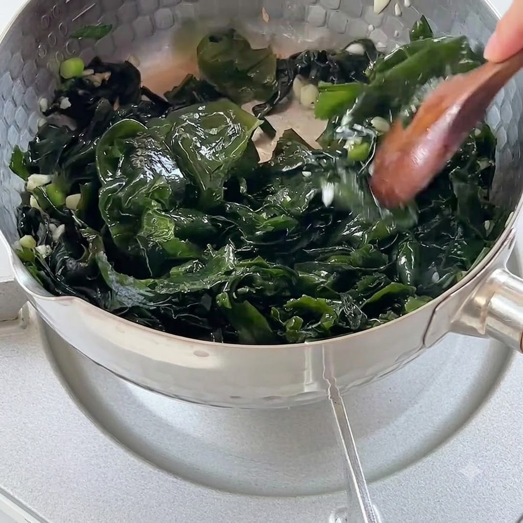 Kochendes Wasser wird in einen Topf mit angebratenen Algen und Aromaten gegossen.