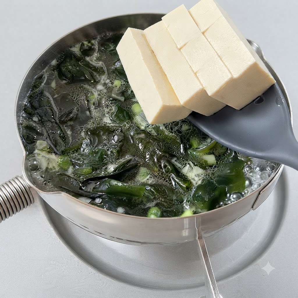 Tofuwürfel werden mit einem Schaumlöffel in einen sprudelnden Topf mit Algensuppe gegeben.
