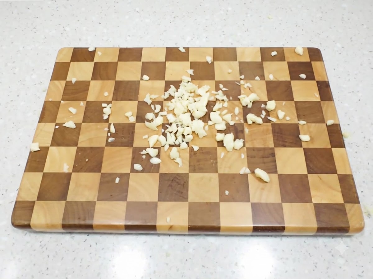 Fein gewürfelte Knoblauchzehen auf einem karierten Holzschneidebrett.