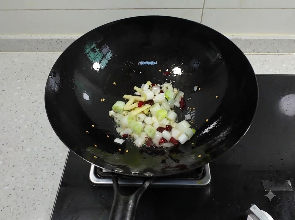 Gehackte Frühlingszwiebeln, Ingwer, Knoblauch und getrocknete Chilis brutzeln in einem schwarzen Wok mit heißem Öl.
