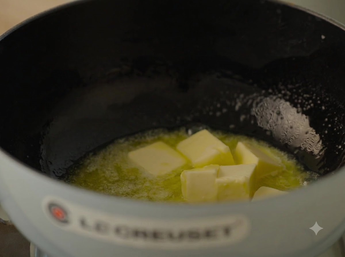 Große Stücke ungesalzene Butter schmelzen und blubbern in einem hellblauen Gusseisentopf.