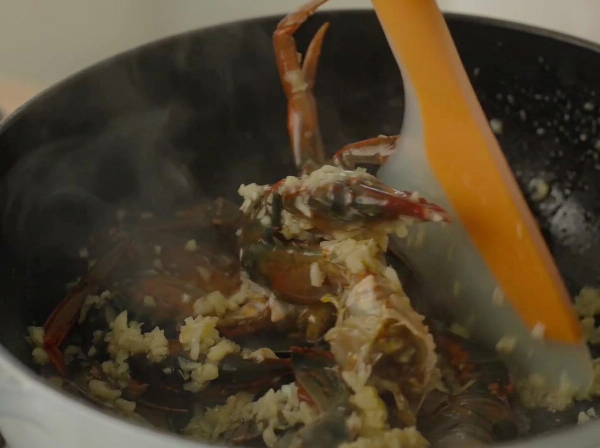 Ein Silikonspatel rührt Krabben und Garnelen in einem dampfenden Topf um.