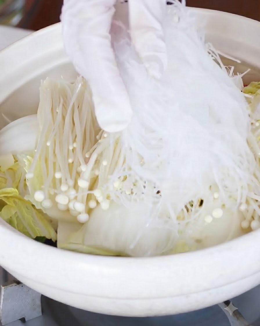 Eingeweichte Glasnudeln werden über die Schicht aus Enoki-Pilzen und Kohl gelegt.