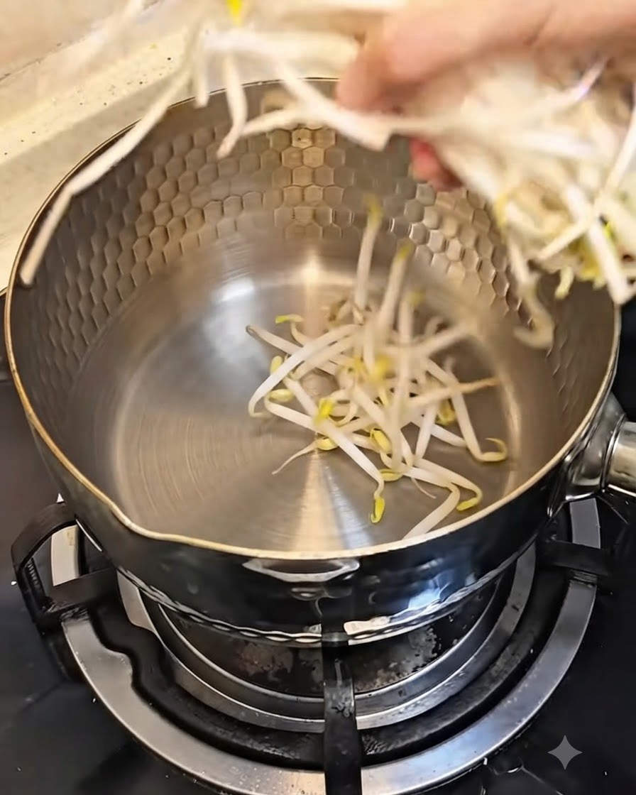 Eine Hand legt eine Handvoll frischer Bohnensprossen in einen sauberen Metalltopf.