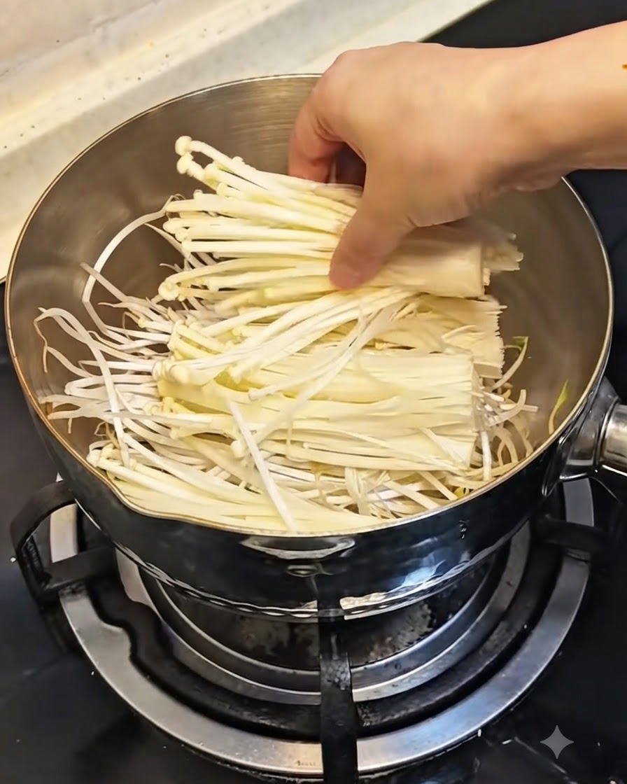 Eine Hand legt ein Bündel frischer weißer Enoki-Pilze über die Sprossen in den Topf.